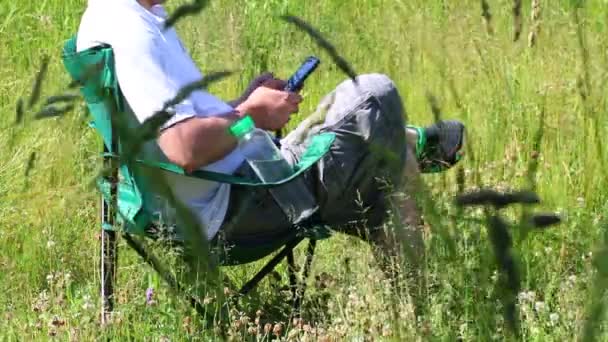 Uomo Seduto Una Sedia Picnic Pieghevole Lavora Con Uno Smartphone — Video Stock
