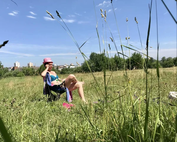 Yeşil çayırda güneşlenmek için mayo giyerek bir kız. Bir piknik için katlanır sandalyede oturur.