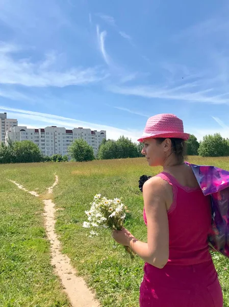 Kız yol boyunca yürüyor, bir buket Chamomiles tutuyor. Yol konut Massif için yüksek yeşil çim ile bir çayır aracılığıyla yol açar.