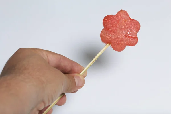 Pieces of the pulp of watermelon are cut with a stamp. They are given different forms. Stringed on skewers for a picnic. The man is holding one skewer in his hand.