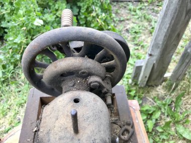 El sürücü eski dikiş makinesi yakın çekim. Korozyon, toz ve örümcek ağları ile kaplı. Terk edilmiş ahşap bir ahır arka planı.