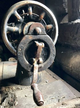 El sürücü eski dikiş makinesi yakın çekim. Korozyon, toz ve örümcek ağları ile kaplı. Terk edilmiş ahşap bir ahır arka planı.