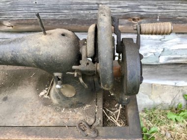 El sürücü eski dikiş makinesi yakın çekim. Korozyon, toz ve örümcek ağları ile kaplı. Terk edilmiş ahşap bir ahır arka planı.