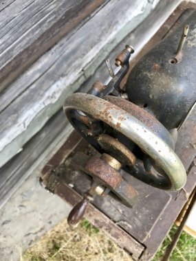 El sürücü eski dikiş makinesi yakın çekim. Korozyon, toz ve örümcek ağları ile kaplı. Terk edilmiş ahşap bir ahır arka planı.