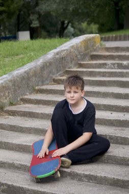 Bir kaykay ile bir genç. Bir taş merdiven zemin karşı bir kaykay ile oturur.