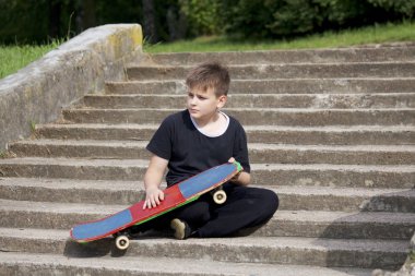 Bir kaykay ile bir genç. Bir taş merdiven zemin karşı bir kaykay ile oturur.