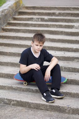 Bir kaykay ile bir genç. Bir taş merdiven zemin karşı bir kaykay üzerinde oturur.