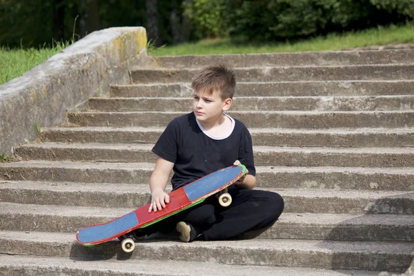 Adolescente Con Una Patineta Sienta Con Monopatín Sobre Telón Fondo — Foto de Stock