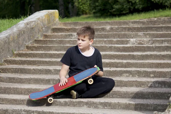 Bir kaykay ile bir genç. Bir taş merdiven zemin karşı bir kaykay ile oturur.
