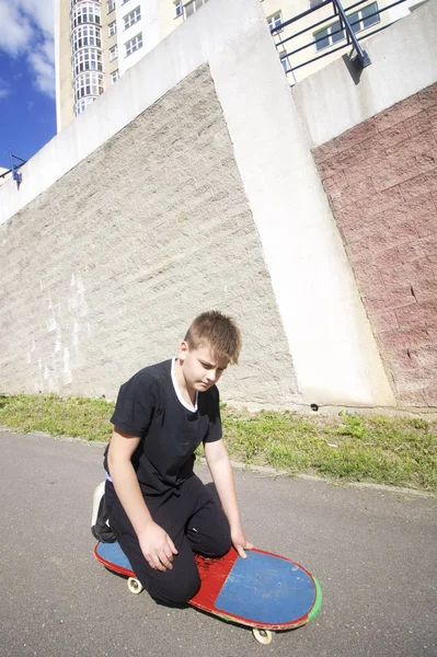 Bir kaykay ile bir genç. Bir kaykay üzerinde oturur.