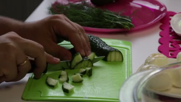 一个男人从盘子里拿出一根黄瓜 然后开始在切板上切 附近的菜肴是其他烹调的配料 鸡蛋和莳萝 — 图库视频影像
