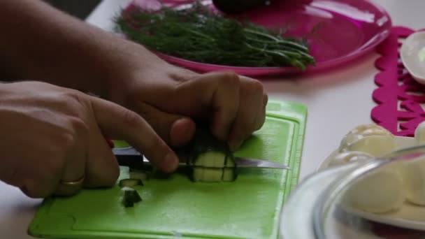 一个男人从盘子里拿出一根黄瓜 然后开始在切板上切 附近的菜肴是其他烹调的配料 鸡蛋和莳萝 — 图库视频影像