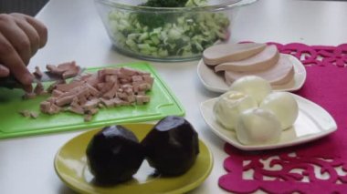 Aşçı haşlanmış sosis kesme tahtası üzerinde keser. Yakındaki içinde bulaşıkları şeker pancarı, tavuk yumurta, sosis ve salatalık yemek pişirmek için diğer unsurlarıdır. Yukarıdan görüntülemek.