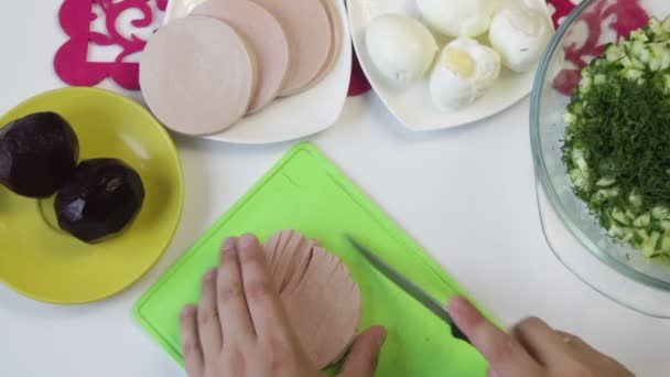 料理は まな板の上のボイル ソーセージをカットします 近くの料理は 砂糖大根 鶏の卵 ソーセージ きゅうりを調理するための他の原料 上からの眺め — ストック動画