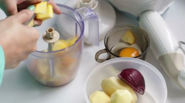 Kadın sebze taşlama için bir blender içine kabak pirzola. Konteyner yanında patates ve soğan var. Cam bir tavuk yumurta.