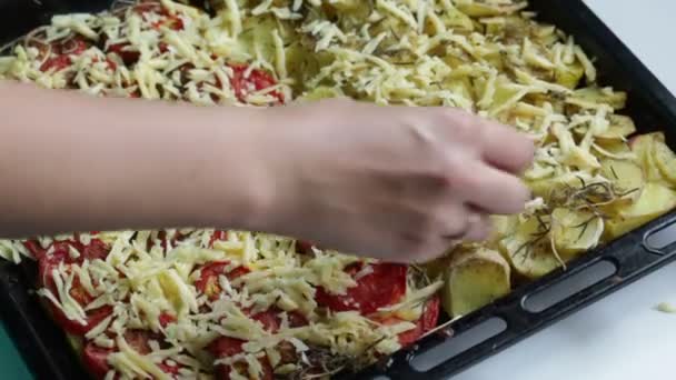 女性は ベーキング トレイにみじん切りのチーズを振りかけます 鍋にトマト ズッキーニ ジャガイモを置いた — ストック動画
