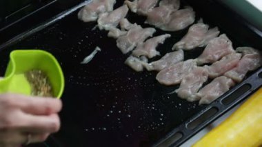 Akşam yemeği yemek için malzemeler. Kadın tavuk fileto parçaları fırın tepsisine koyar ve baharatlarla sprinkles.