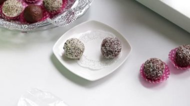 Bir kadın kakao tozu ve çerezleri tatlılar yapıyor. Susam ve Hindistancevizi talaşı serpin. Hazır tatlılar tabaklar, plastik film üzerinde boş yalan yalan.