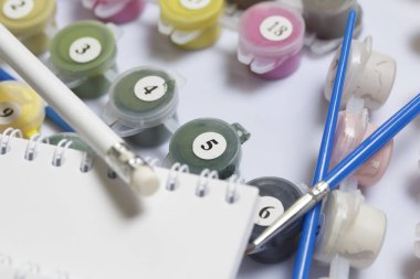 Kapları boyalar ve farklı boyutlarda fırçalar ile numaralandırılmış. Numaraları çizerek için. Not defteri ve kalem çizimler için. Beyaz bir arka plan üzerine döktüm.