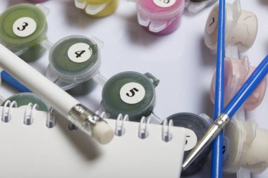 Kapları boyalar ve farklı boyutlarda fırçalar ile numaralandırılmış. Numaraları çizerek için. Not defteri ve kalem çizimler için. Beyaz bir arka plan üzerine döktüm.