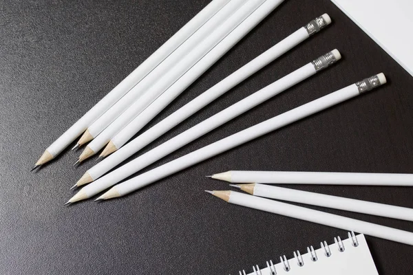 White spring pads and simple pencils for notes and sketches. Stationery for school and teaching. On a dark background.