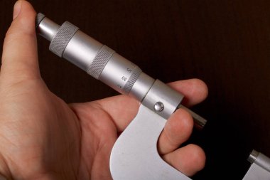 Dış ölçüler ve 25-50 mm ölçüm aralığı için mikrometre ile dairesel bir ölçek. Adamın elinde. Karanlık bir arka plan üzerinde.