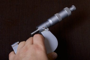 Dış ölçüler ve 25-50 mm ölçüm aralığı için mikrometre ile dairesel bir ölçek. Adamın elinde. Karanlık bir arka plan üzerinde.