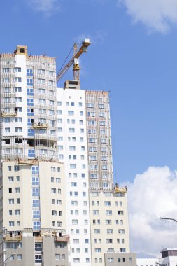 Kule vinç mavi gökyüzüne karşı bina. Vinçler, dış dekorasyon için binanın duvarında asılı. Binalar inşaat altında görülebilir.