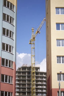 Kule vinç mavi gökyüzüne karşı bina. Hazır evler arasındaki boşluğu içinde görünür. Binalar inşaat altında görülebilir.
