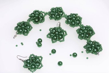 Küpe ve bilezik el yapımı. İğne işi evde. Boncuk takı. Yeşil renkli. Beyaz bir arka plan üzerinde. Boncuk yakın dağılmış.