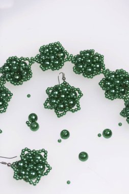 Küpe ve bilezik el yapımı. İğne işi evde. Boncuk takı. Yeşil renkli. Beyaz bir arka plan üzerinde. Boncuk yakın dağılmış.