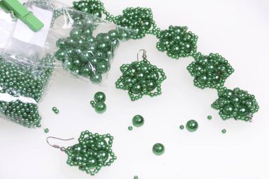 Küpe ve bilezik el yapımı. İğne işi evde. Boncuk takı. Yeşil renkli. Beyaz bir arka plan üzerinde. Boncuk yakın dağılmış.