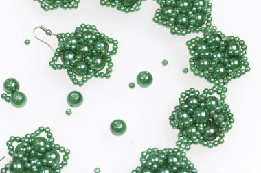 Küpe ve bilezik el yapımı. İğne işi evde. Boncuk takı. Yeşil renkli. Beyaz bir arka plan üzerinde. Boncuk yakın dağılmış.