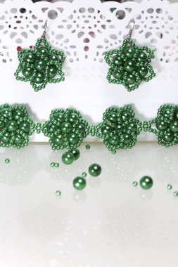 Küpe ve bilezik el yapımı kürsüye asmak. İğne işi evde. Boncuk takı. Yeşil renkli. Beyaz bir arka plan üzerinde. Boncuk yakın dağılmış.
