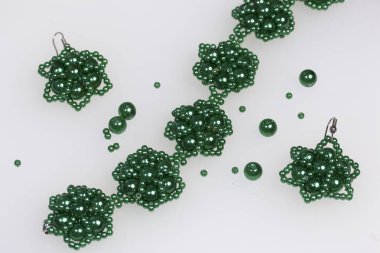 Küpe ve bilezik el yapımı. İğne işi evde. Boncuk takı. Yeşil renkli. Beyaz bir arka plan üzerinde. Boncuk yakın dağılmış.