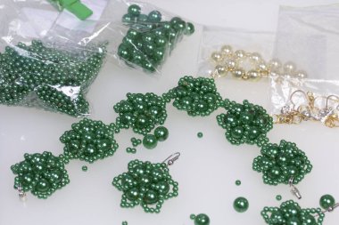 Küpe ve bilezik el yapımı. İğne işi evde. Boncuk takı. Yeşil renkli. Beyaz bir arka plan üzerinde. Boncuk yakın dağılmış.