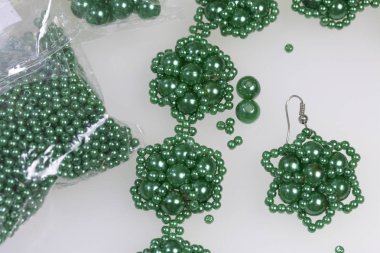 Küpe ve bilezik el yapımı. İğne işi evde. Boncuk takı. Yeşil renkli. Beyaz bir arka plan üzerinde. Boncuk yakın dağılmış.