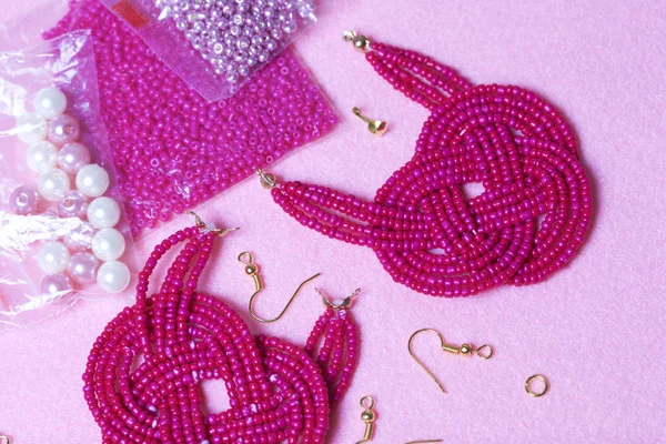 Earrings from beads handmade. Pink colour. Nearby are scattered ear wires and other accessories. Needlework at home. Bead jewelery.