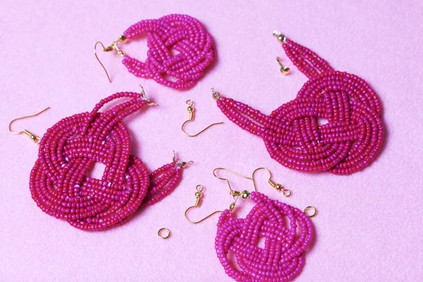 Earrings from beads handmade. Pink colour. Nearby are scattered ear wires and other accessories. Needlework at home. Bead jewelery.