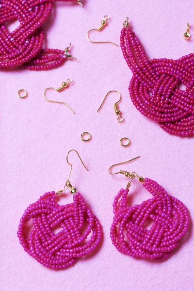 Earrings from beads handmade. Pink colour. Nearby are scattered ear wires and other accessories. Needlework at home. Bead jewelery.