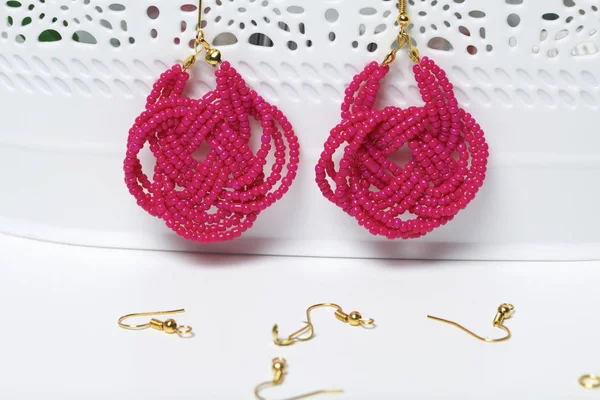 Earrings from beads handmade. Pink colour. Hang on the stand. Nearby are scattered ear wires and other accessories. Needlework at home. Bead jewelery.