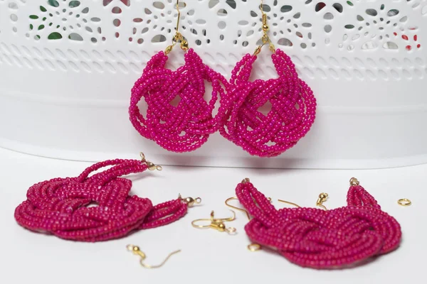 Earrings from beads handmade. Pink colour. Hang on the stand. Nearby are scattered ear wires and other accessories. Needlework at home. Bead jewelery.