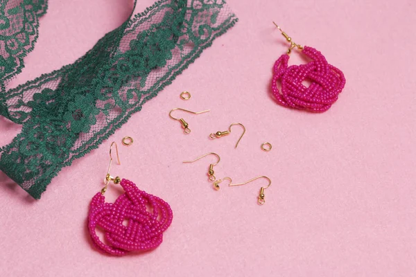 Earrings from beads handmade. Pink colour. Nearby are scattered ear wires and other accessories. Needlework at home. Bead jewelery.