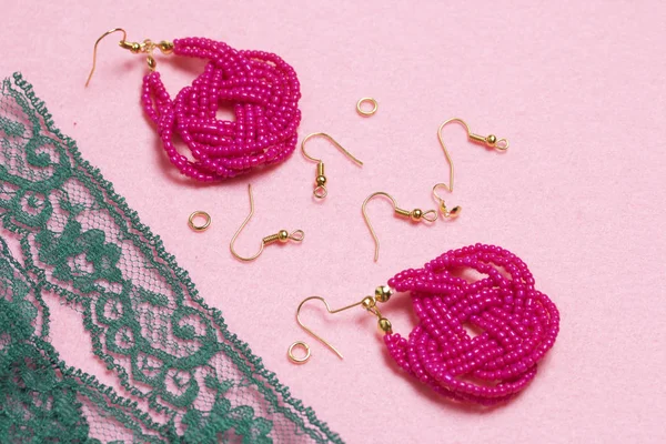 Earrings from beads handmade. Pink colour. Nearby are scattered ear wires and other accessories. Needlework at home. Bead jewelery.