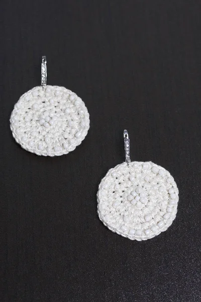 Earrings knitted with embroidery from beads. White color. Handmade. On a dark background.