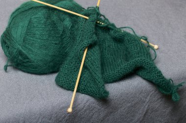 İle ahşap örgü örgü. Koyu yeşil iş parçacığı ve ahşap örgü iğneleri bitmemiş bir örgü içinde bir top.