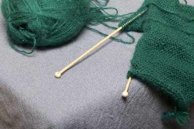 İle ahşap örgü örgü. Koyu yeşil iş parçacığı ve ahşap örgü iğneleri bitmemiş bir örgü içinde bir top.