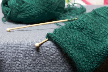 İle ahşap örgü örgü. Koyu yeşil iş parçacığı ve ahşap örgü iğneleri bitmemiş bir örgü içinde bir top.