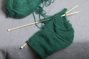 İle ahşap örgü örgü. Koyu yeşil iş parçacığı ve ahşap örgü iğneleri bitmemiş bir örgü içinde bir top.