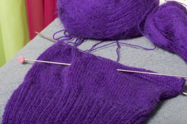 Çelik örgü iğneleri ile örgü. Bir top mor iplik ve bitmemiş bir örme çelik örgü iğneler.